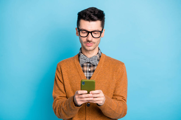 Photo of cute serious young man hand wear brown cardigan spectacles chatting modern gadget isolated blue color background - Photo, image