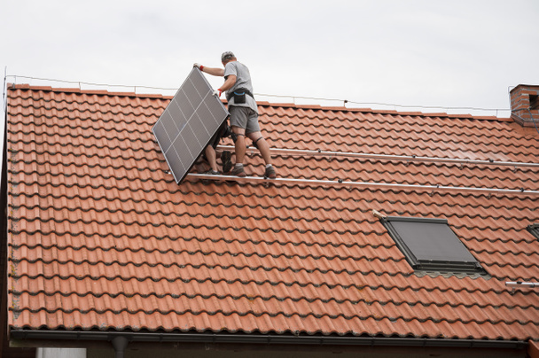 Dos ingenieros en el techo de la casa ensamblan el panel fotovoltaico. - Foto, Imagen