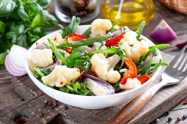 Saláta arugulával, pörkölt zöldségekkel (karfiol, vörös harangbors és hagyma) és magvakkal. Egészséges élelmiszer. - Fotó, kép