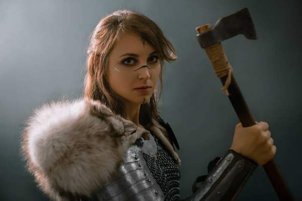 Portrait of a medieval fantasy female warrior in armor armed with an ax, posing in the studio in the dark on a black background. - Foto, afbeelding