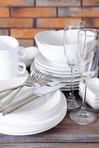 Set of white dishes on table on brick-wall background - Foto, afbeelding