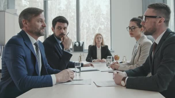 Lentitud media de dos hombres de negocios exitosos y sus abogados sentados en la mesa de negociaciones en la moderna sala de oficina estrechando las manos después de hacer un trato - Imágenes, Vídeo
