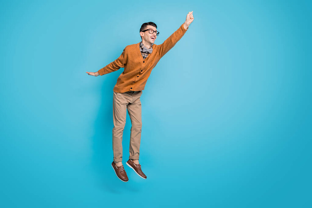 Full body photo of young excited man try catch umbrella jump up look empty space isolated over blue color background - Foto, Imagem