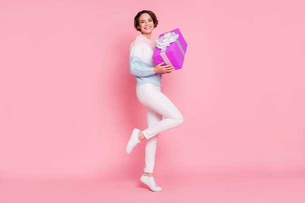 Photo portrait full body view of woman standing on one leg holding big purple present isolated on pastel pink colored background - Photo, image