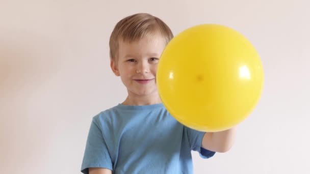 Πορτρέτο του χαριτωμένο μικρό αγόρι παίζει με κίτρινο μπαλόνι αέρα καουτσούκ χαλαρωτικό έχοντας θετικό συναίσθημα - Πλάνα, βίντεο