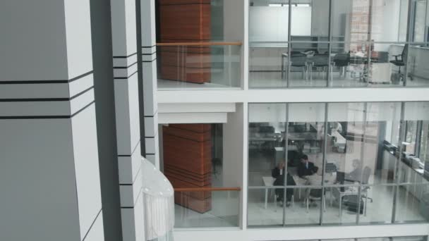 PAN shot van team van professionele adviseurs zitten rond tafel in glazen vergaderzaal op de eerste verdieping van modern kantoor - Video