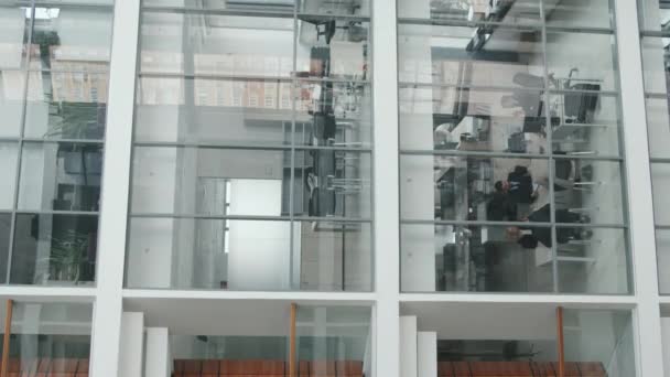 Verticale shot van modern kantoor met zakenmensen die vergaderen in een glazen vergaderzaal op de eerste verdieping - Video