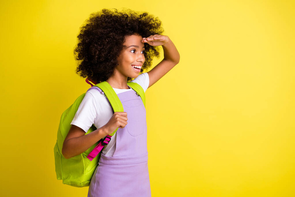 Profile photo of little girl look empty space palm forehead wear bag purple overall isolated yellow color background - Fotó, kép