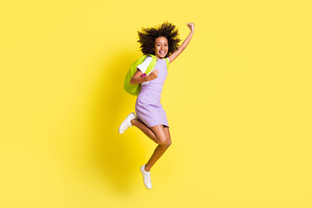 Full size photo of optimistic cute curly girl jump wear rucksack t-shirt dress isolated on yellow color background - 写真・画像