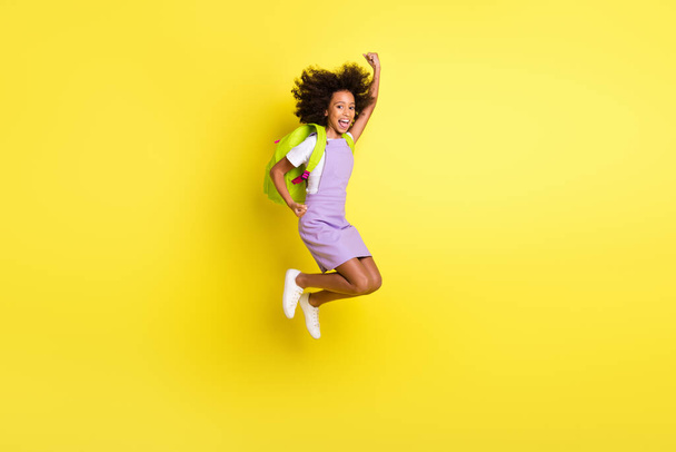 Full length body size photo of funny schoolgirl jumping high gesturing like winner wearing backpack isolated bright yellow color background - Fotografie, Obrázek
