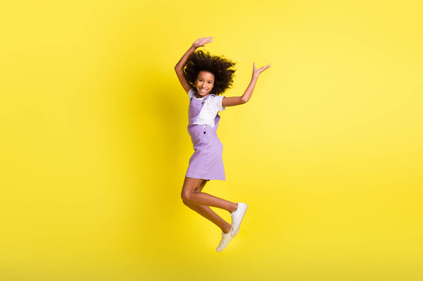 Full length body size photo of funny child jumping high carefree laughing in purple overall isolated vibrant yellow color background - Foto, imagen