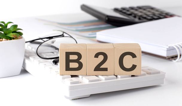 B2C escrito en cubo de madera en el teclado con herramientas de oficina - Foto, Imagen
