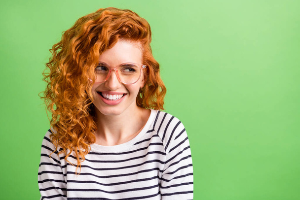 Photo of pretty funny young lady dressed striped clothes glasses looking empty space smiling isolated green color background - Foto, Bild