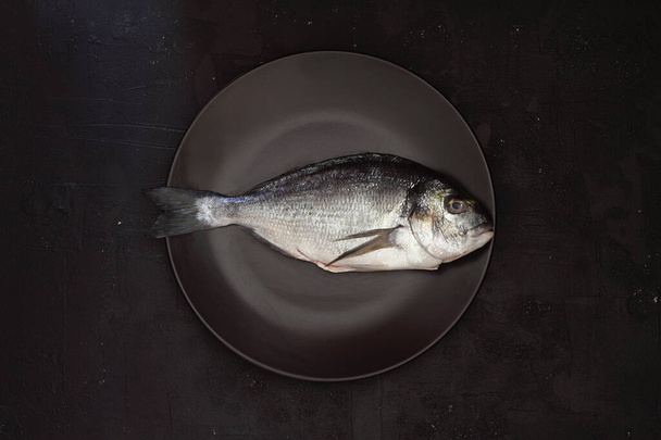 fresh fish on a black wooden board. Raw uncooked sea bream on black plate. - Foto, afbeelding
