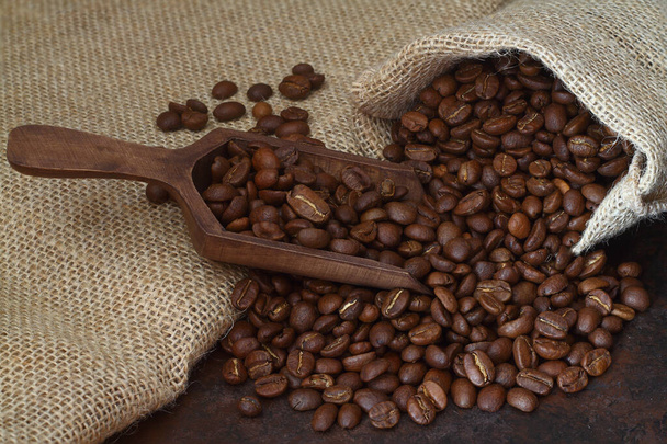 Granos de café tostados de cerca en cucharada de madera en el saco de arpillera de fondo, enfoque selectivo - Foto, Imagen