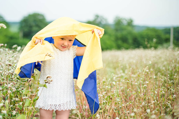Flagge der Ukraine in den Händen eines lächelnden kleinen Mädchens. Glückliches Kind trägt gelb-blaue Fahne. Tag der Unverwüstlichkeit der Ukraine. Selektiver Fokus auf Flagge - Foto, Bild