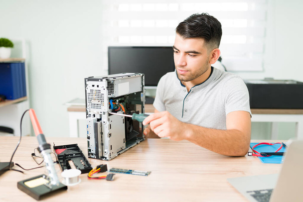 Giovane tecnico maschio che installa nuovi componenti su una CPU rotta per un cliente. Uomo latino che gestisce un'officina di riparazione - Foto, immagini