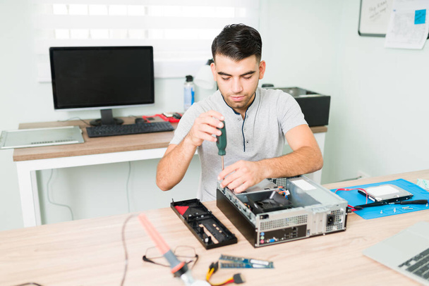 Homem latino focado usando uma chave de fenda para desmontar os componentes de um computador CPU. Técnico masculino trabalhando na reparação de hardware - Foto, Imagem