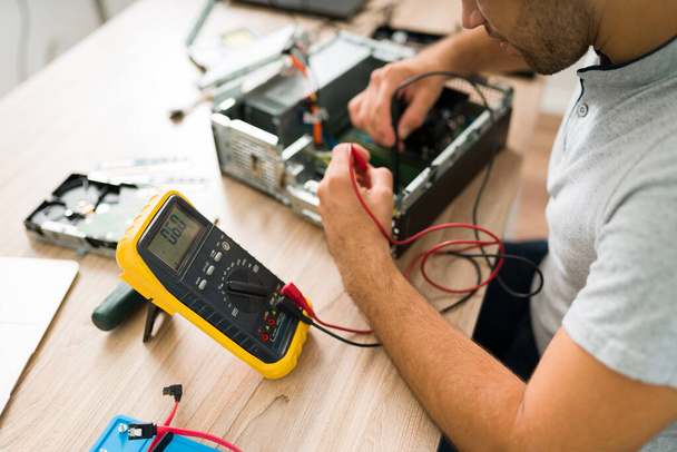 Technician using a multimeter to measure the voltage of a broken computer. Young man checking the computer connections at the repair shop - Foto, Imagem