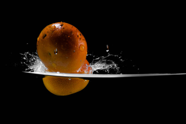Mandarin falls into water creating spray on a black background, copy space - Photo, Image