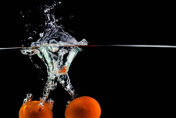 two tangerines fall into the water on a black background, copy space - Valokuva, kuva