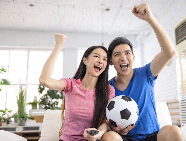 Young couple watching tv and  raising hands to celebrating the victory - Фото, зображення