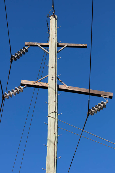 Foto van een houten telefoonpaal en kabels tegen een blauwe lucht - Foto, afbeelding
