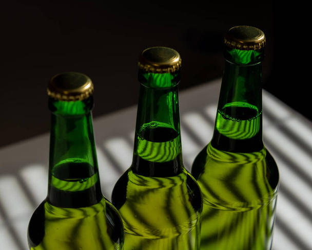 Three green glass beer bottles in the shade of the blinds. - Zdjęcie, obraz