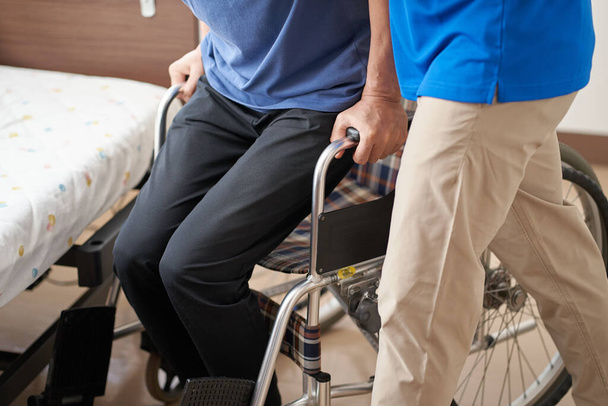 Verzorger assisteert ouderen in een rolstoel - Foto, afbeelding