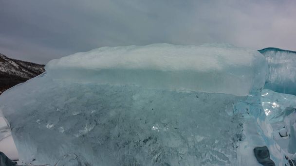 曇り空を背景にターコイズ色の氷のハンモック。接近中だ。テクスチャ。詳細は？。端に太陽の輝き。表面に雪。バイカル - 写真・画像