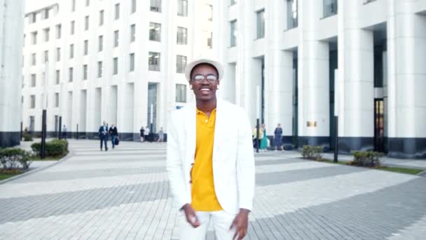 Hymyilevä musta mies valkoisessa puvussa tanssii musiikkia kuunnellen - Materiaali, video