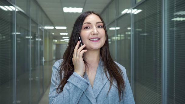 Brunette businesswoman in grey jacket talks on smartphone - 写真・画像