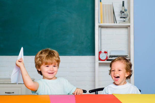 Cute little preschool kid boy study in a classroom. Educational process. Elementary school and education. Funny toddlers from elementary school hold paper plane laughing and smiling. - Foto, Bild