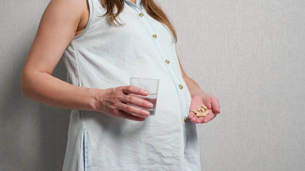 Mujer embarazada irreconocible sosteniendo la medicina en una mano y en otro vaso de agua - Foto, imagen