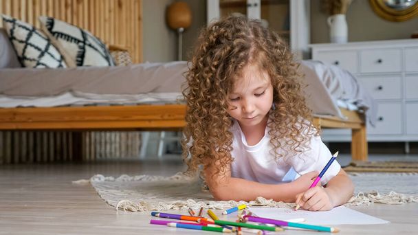Pequena menina pré-escolar com longos cabelos encaracolados soltos desenha - Foto, Imagem