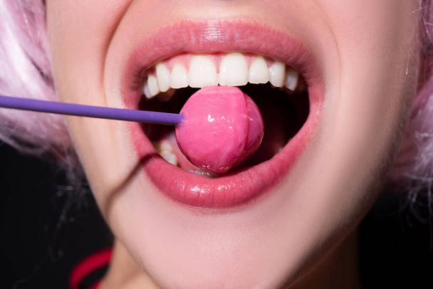 Sensual red lips with candy for print. Red lollipop in the mouth in art design. Glossy womans lips licking sucking lollipop. Sensual sexy mouth with candy concept enjoyment beautiful female lips. - Foto, imagen