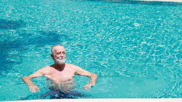 felice anziano caucasico nuotare in piscina durante la vacanza di pensionamento con relax e sorridente - Foto, immagini
