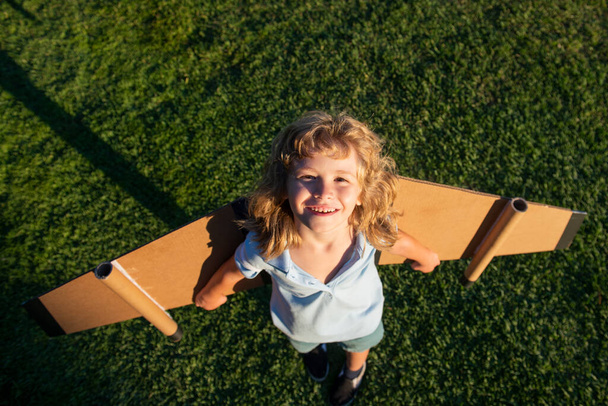 Top view child playing with toy plane wings in summer park. Innovation technology and success concept. Kid pilot having fun on grass in park. - Φωτογραφία, εικόνα