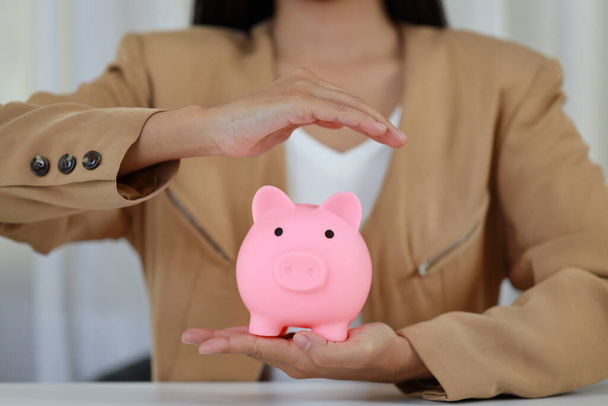 Young active business woman hands in casual dress sitting and protecting piggy bank on white table. Insurance and security concep - Foto, immagini