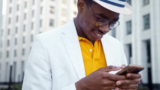 Homem negro alegre em óculos e tipos de terno no smartphone - Filmagem, Vídeo