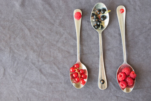 Grosella roja y negra y loganberries en la cuchara de hierro en el fondo gris. Gran grupo de bayas de colores. - Foto, Imagen