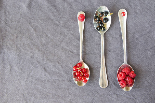 Grosella roja y negra y loganberries en la cuchara de hierro en el fondo gris. Gran grupo de bayas de colores. - Foto, imagen