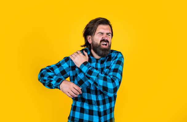 brutal bearded hipster feel pain. mature guy with moustache on face. expressing human emotions. suffering man in checkered shirt. man has ache in shoulder on yellow background - Zdjęcie, obraz