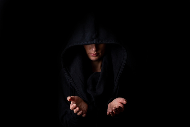 Mujer joven con capucha negra y palmas abiertas sobre fondo negro oscuro.  - Foto, Imagen