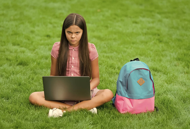 upset kid while using computer sit on green grass in park with school bag, childhood education - Foto, Imagem