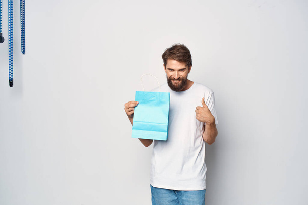 man in white t-shirt blue package shopping light background - Foto, imagen