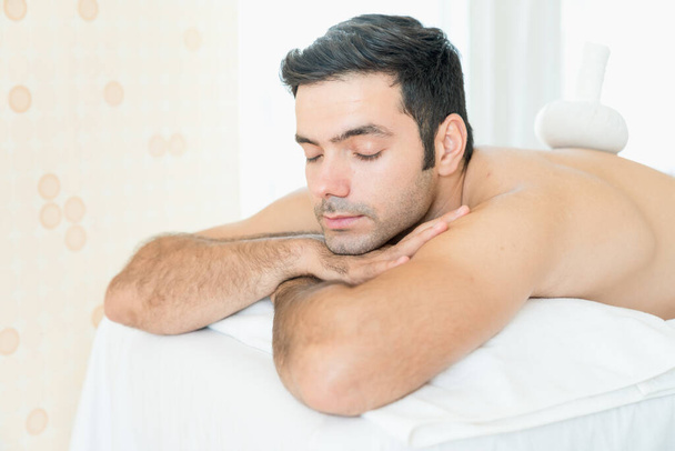Junger Mann schläft bei Wellness-Massage. Mann massiert Klient mit Kräuterbällchen im Liegen auf Massagetisch. - Foto, Bild