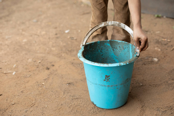 The child is holding a bucket. Blue bucket in hand. The boy plays with a bucket and a shovel. A child stained his clothes while playing in the yard. - Foto, afbeelding