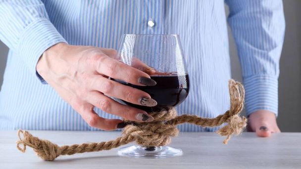female hand holding wine glass is tied with a jute rope. The concept of alcohol dependence. - Photo, Image