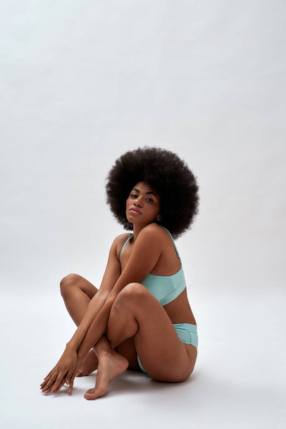Playful young woman with afro hairstyle sitting on floor - Foto, imagen